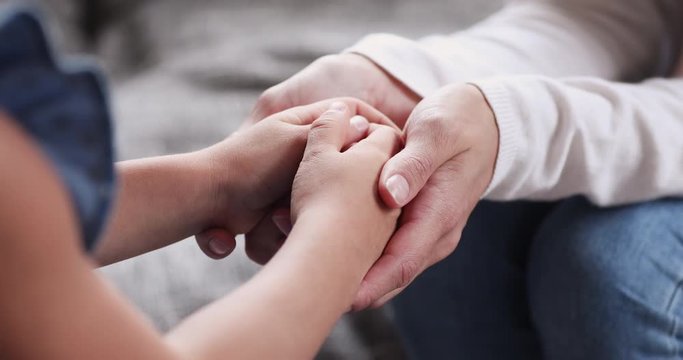 Closeup of child daughter holding adult foster care mother hands
