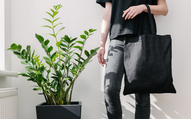 Young woman holding black textile eco bag againstwhite wall. Ecology or environment protection...