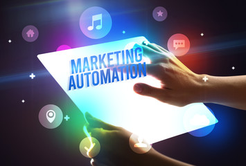 Holding futuristic tablet with MARKETING AUTOMATION inscription, new technology concept