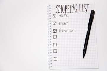 Naklejka premium Shopping list. Squared notebook with black pen on a white background. Record ideas, notes, plans, tasks. The list includes bread, milk, bananas. Copy Spase