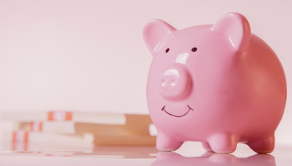 Pink piggy bank against money backgrouund as symbol of profit and success. Horizontal image.