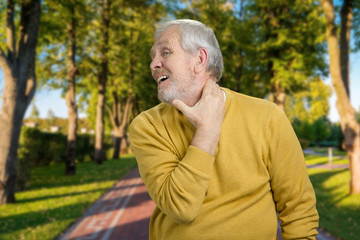 Old grandpa having neckache in the park. Grandfather feels pain in summer park.