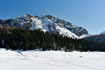 Fototapeta na wymiar Palù lake ice in winter with snowmobile footprint on the snow.