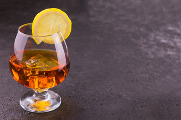 Glass of cognac and lemon slices isolated on black background. Copy space.	