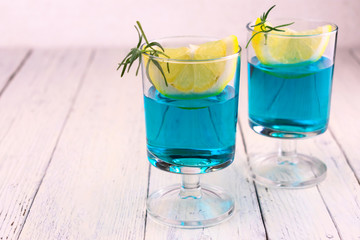  Blue alcoholic cocktail with a slice of lemon on a white wooden background. Copy space.