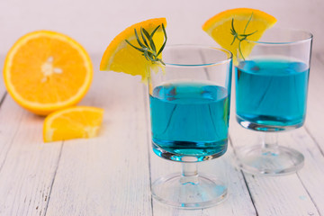Blue alcoholic drink with slices of orange on a white wooden background.