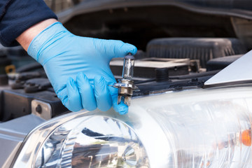 Hand holding a car light bulb, headlamp in the background. Headlight replacement concept.