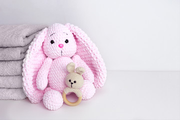 Baby clothes and fluffy pink bunny toy with long ears on white wall background. Copy space.