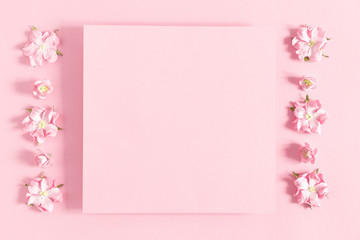 Flowers composition creative. Pink flowers, empty paper on pastel pink background. Flat lay, top view, copy space 
