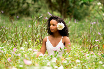 Naklejka na ściany i meble Contact with nature. Beautiful young black woman with curly hair in a flower field. Flower in hair. 
