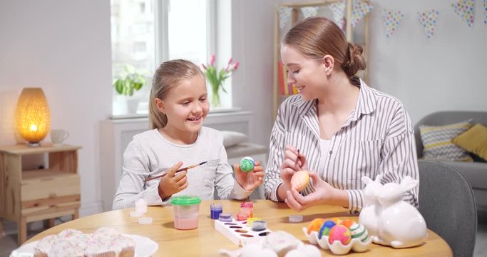 Happy mother and daughter painting eggs for Easter celebration at home