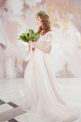 Portrait of a young beautiful woman in wedding dress with wreath and bouquet of fresh flowers.