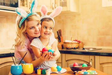 daughter and mother in rabbit costume prepare for Easter and paint eggs