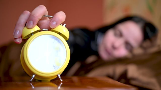 Morning. The alarm clock rings on the bedside table, the girl wakes up in bed and turns off the alarm clock and gets up. New day