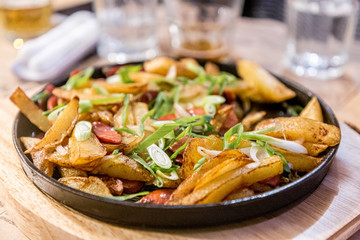 Fried potatoes with sausage on a black cast-iron pan in a restaurant.