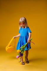 little blonde girl in a straw hat and sunglasses is smiling on a yellow background. child girl in a blue dress is holding a pineapple-shaped drink glass on a yellow background.summer vacation concept