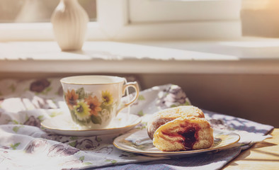 Selective focus of home made jam doughnuts with burry background of cup of hot blueberry tea, Soft focus of afternoon tea served with strawberry jam donut in sunny day summer, English traditional