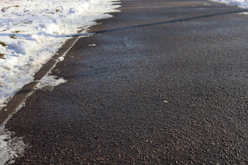 Asphalt path with snow on the sides. Wet asphalt and snow near it