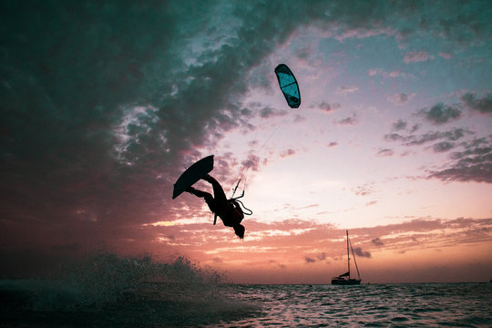 A kitesurfer doing a flip in the setting sun.