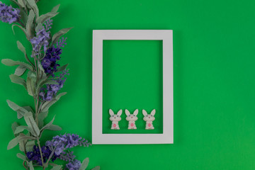 White photo frame and rabbits on medium green paper background for Spring and Easter, Flat lay, top view, copy space.