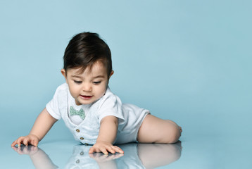 Little child in white bodysuit as a vest with bow-tie, barefoot. He is laying on the floor against blue background. Close up