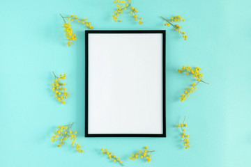 Flowers composition spring. Blank photo frame and mimosa flowers on pastel blue background. Flat lay, top view, copy space