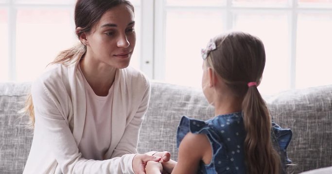 Caring young mom holding hands talking to small child girl