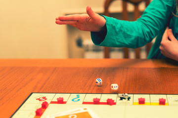 A girl playing a board game and rolls dice. Hand throws the dice on the background of colorful blurred fantasy Board games, gaming moments in dynamics. toned