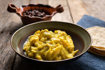 Mexican scrambled eggs with green sauce on wooden background