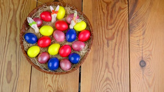 Top view of female hands pose a basket with colorful Easter eggs on a wooden table. Easter decorations. Easter concept background.