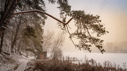 Winter landscape with the forest, frozen river and old wooden bathhouse at the snow blizzard