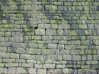 an old grey stone wall made of large irregular blocks covered in patches of moss