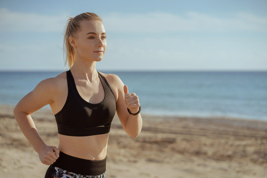 woman running seaside with sport clothers and smart watches on hand; female jogger waist-high view training; sport and fitness concept.
