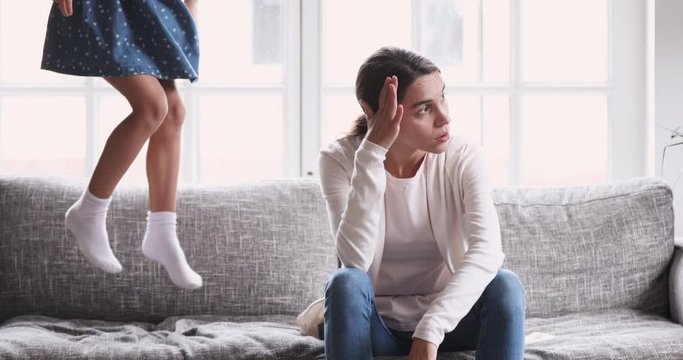 Exhausted young mother tired of hyperactive noisy kid daughter