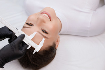 Beautiful young girl with long eyelashes tweezing her eyebrows in a beauty salon. Woman doing...
