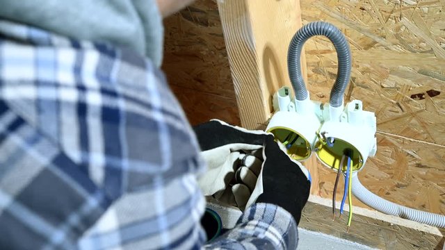 Male Electrician Binds and Organizes Alike Wires In Outlet In New Construction Site. 
