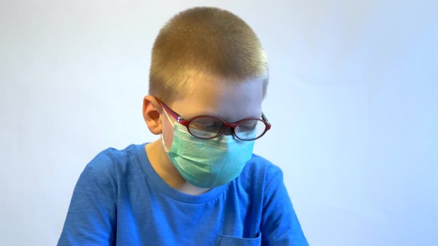 Cute blond boy in quarantine at home. baby in blue medical mask is struggling with illness, fever and strong cough. Epidemic control of coronavirus and proper infection prevention. Child coughs