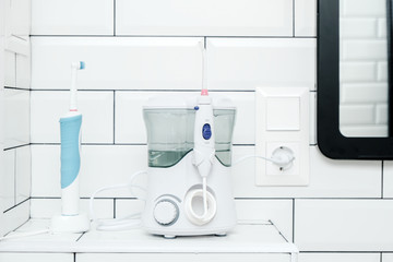 Electric oral irrigator and a rechargeable toothbrush are in the white tiled bathroom, next to the mirror.