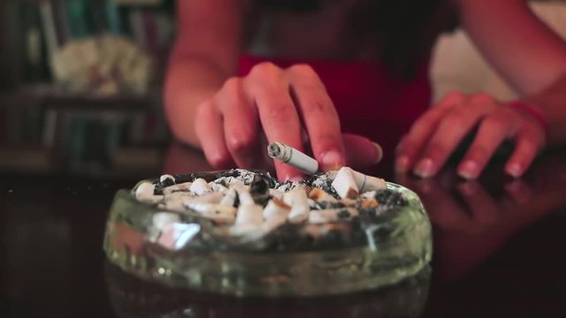 A woman shakes ashes in an ashtray. Shake off the cigarette ashes. Smoking a cigarette. Female hand ashing cigarette into ashtray