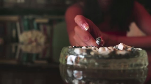 A woman shakes ashes in an ashtray. Shake off the cigarette ashes. Smoking a cigarette. Female hand ashing cigarette into ashtray