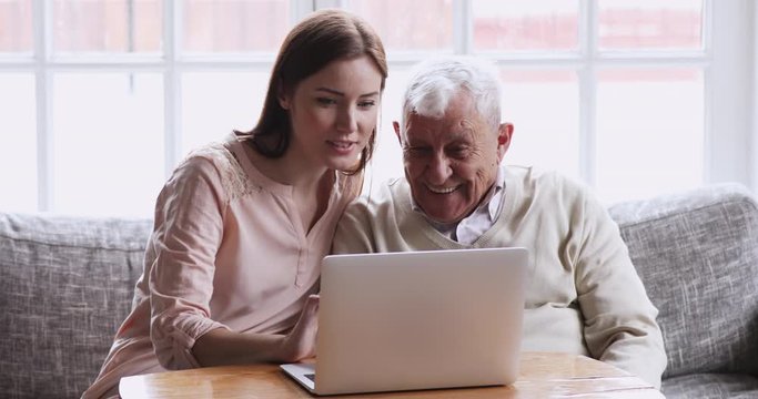 Young adult grown granddaughter helping senior elder grandfather with computer