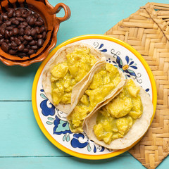 Mexican scrambled eggs tacos with green sauce on turquoise background