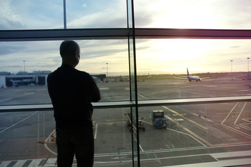 Fototapeta na wymiar man, a passenger, waiting for his flight, stands at the window and looks at the airport runway, a travel concert