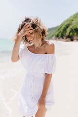 Carefree young lady in summer dress touching her wavy hair. Outdoor photo of happy female model...