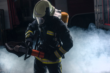 Fototapeta premium Portrait of a fireman wearing firefighter turnouts and helmet. Dark background with smoke and blue light.