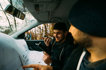Two armed bandits sitting in a car planning their next robbery, while counting on a stopwatch the time they have for the robbery, showing off their guns and pointing at the blueprint.