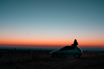 Obraz na płótnie Canvas silhouette of man sitting on a car at sunset