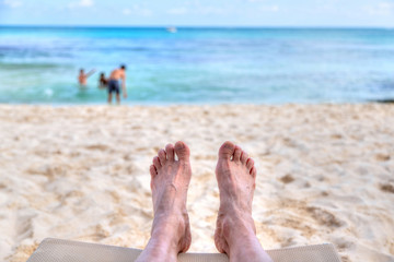 Personal perspective of man relaxing at beach with feet view