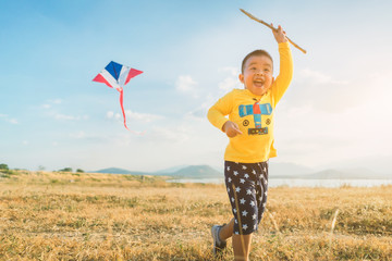 Happy children running with a kites  on meadow in nature amid the golden light of the sunset. There are lakes and mountains at the background.