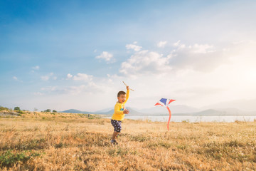 Happy children running with a kites  on meadow in nature amid the golden light of the sunset. There are lakes and mountains at the background.